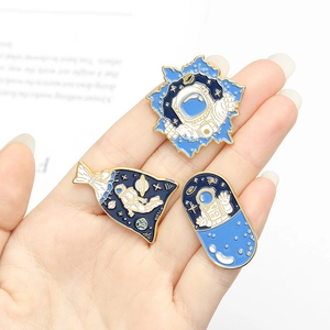 Close-up of three enamel astronaut pins in blue and gold on a minimal white background