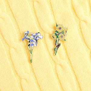 Detail of enamel sunflower and iris flower brooches on yellow knitted fabric background