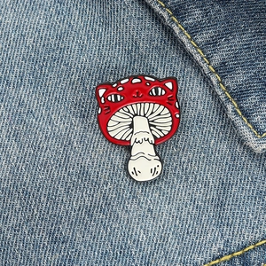 Detailed macro of a creative red mushroom and cat enamel pin on dark blue denim jacket