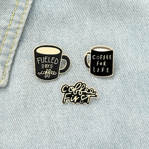 Dettaglio di tre spille in smalto a tema caffè con slogan su tessuto denim blu
