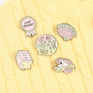 Détail de cinq pin's en émail overthinker sur un pull en maille jaune pastel