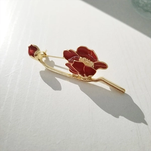 Detailed view of red enamel lily flower brooch on branch with gold metallic finish