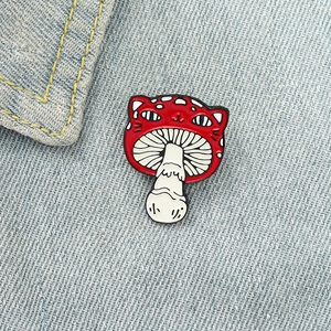 Close-up of a cute cat-headed red mushroom enamel pin on a blue denim jacket pocket