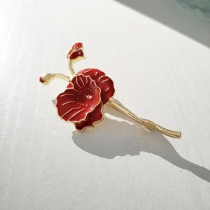 Detail of red enamel poppy brooch with gold metal petals and blooming floral buds