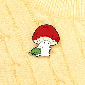 Close-up of enamel red mushroom and green frog pin on a cozy yellow knit background