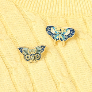 Detail of two butterfly enamel brooches with celestial symbols on yellow knit sweater