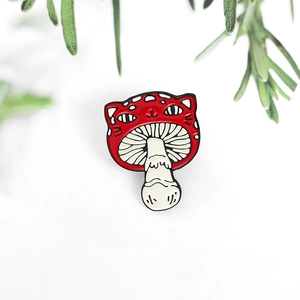 Detail of red cat-shaped mushroom enamel pin with cat ears and white polka dots on it