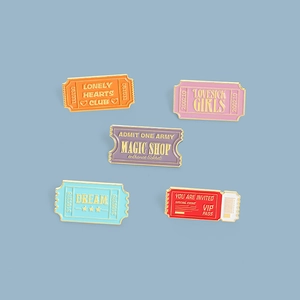 Macro detail of retro stamp-shaped enamel ticket pins with gold-plated edges in five colors