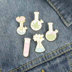 Minimalist pink daisy and lab glassware enamel pin set on a blue denim jacket pocket