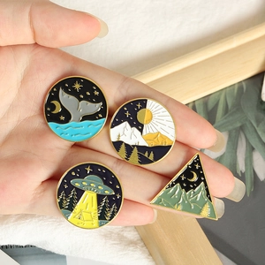 Detailed macro view of four creative enamel pins held by hand showing size and vibrant colors