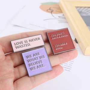 Three colorful enamel pin badges with inspirational quotes held in hand in warm lighting
