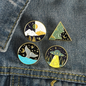 Creative enamel pin set featuring whale tail, mountain, and UFO designs on denim jacket