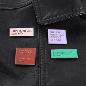 Close-up of colorful enamel pins with English slogans on a black leather jacket collar