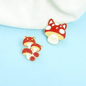 Detail view of two cute cat-eared red mushroom enamel pins with golden metal edges