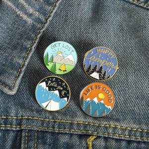 Set of four circular outdoor camping enamel pins with mountain and forest scenes