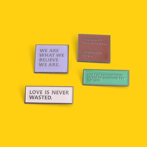 Colorful alloy enamel pins with motivational quotes on a vibrant yellow background