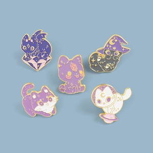 Detail view of five cartoon enamel cat pins with wizard hats and celestial star patterns
