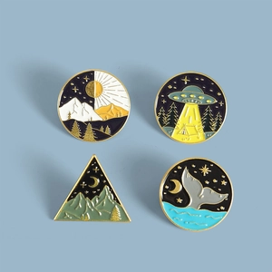 Detail of four creative enamel pins with whale tail and UFO forest landscape themes