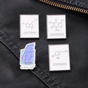 Dettaglio di 4 spille smaltate scientifiche con serotonina e dopamina su pelle nera