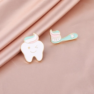 Macro detail of tooth and toothbrush enamel pins on soft pink satin fabric