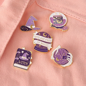 Detailed close-up of 5 purple enamel pins with magic themes on pink denim fabric