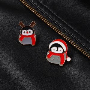Détail de deux jolies broches pingouins de Noël en émail sur un fond de cuir noir
