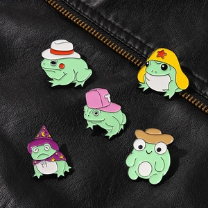 Detail showing five cute green frog enamel pins with colorful hats on a black leather jacket