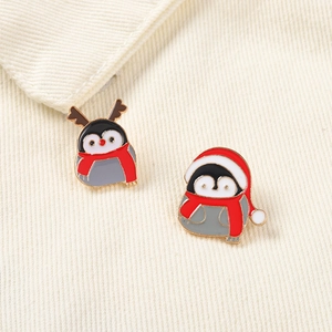 Détail de pins pingouin en émail avec bonnet de Noël et bois de renne sur tissu blanc