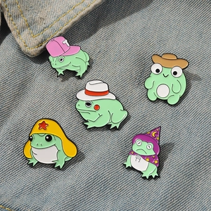 Detail view of five assorted cartoon frog enamel pins on blue denim fabric background