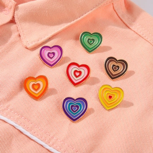 Detailed view of colorful rainbow heart enamel pins on light fabric texture