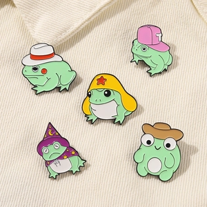 Detailed macro shot of five green enamel frog pins with colorful hats on corduroy