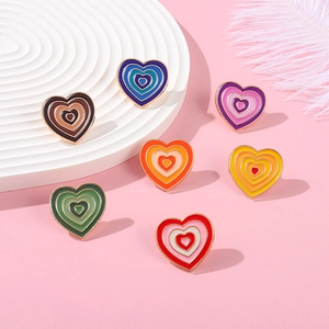 Close-up of rainbow gradient heart enamel pins with gold trim on pink background