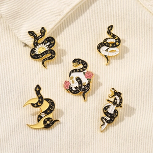 Detail of five unique snake enamel pins with celestial moon, sun and rose motifs on beige fabric
