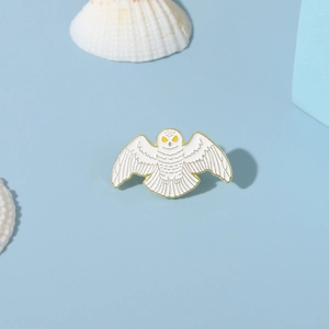 Cute white owl enamel brooch pin with golden wings shown on a shell background