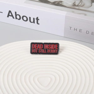 Close-up of Dead Inside enamel pin on a white textured plate with a book background