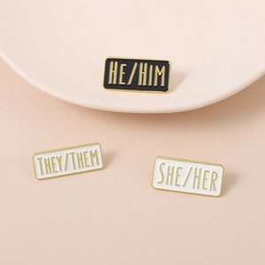 Macro view of alloy enamel rectangle pins featuring HE HIM THEY THEM and SHE HER pronouns