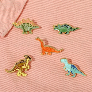Detailed macro of five colorful cartoon dinosaur enamel brooches on pink denim fabric