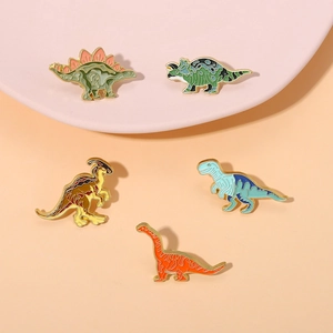 Set of five colorful dinosaur enamel pins with golden metal edges on a tray