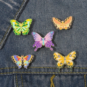 Détail de cinq broches papillon colorées en émail sur fond de tissu en denim bleu
