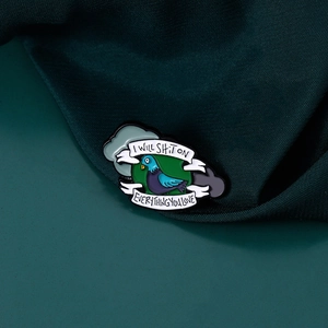Pin's en émail pigeon humoristique avec citation sur fond en tissu vert foncé