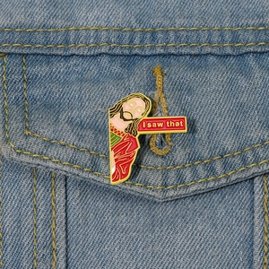Funny Jesus enamel pin with 'I saw that' text on a denim jacket pocket edge