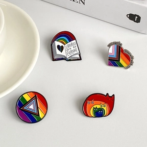 Nahaufnahme von vier Regenbogen-Emaille-Pins mit inklusiven Slogans auf weißem Tisch