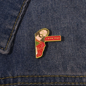 Close-up of 'I saw that' Jesus enamel pin on dark blue denim jacket fabric