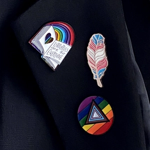 Set aus drei Emaille-Pins mit Bibliotheksbuch, Feder und Pride-Kreis auf schwarzem Revers