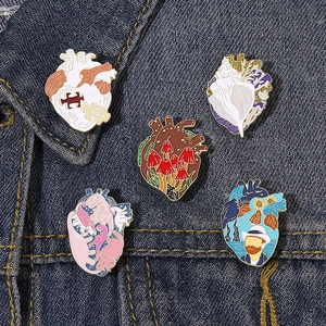 Five unique artistic anatomical heart enamel pins set displayed on dark denim fabric