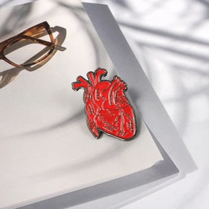 Anatomische rote Herz-Emaille-Brosche mit schwarzen Nickelrändern auf einem Buch