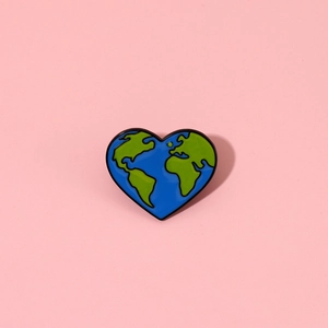 Close-up of heart-shaped enamel pin featuring a green and blue world map design