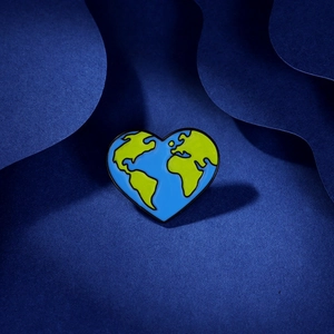 Artistic detail of heart-shaped earth enamel pin with blue oceans on wavy background