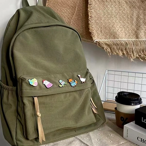 Detail of five colorful cartoon enamel animal pins on a green canvas backpack