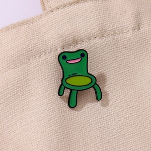 Creative green frog chair alloy enamel brooch pinned on a beige textured canvas bag
